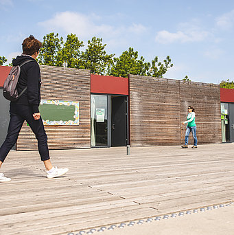 Zwei Frauen laufen am Umweltbildungszetrum mit Holzfassade im Kienberpark vorbei